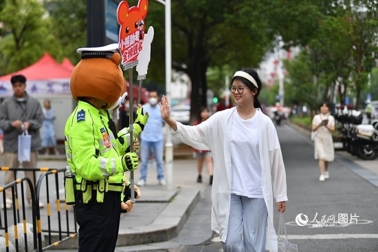6月7日上午9時，隨著鈴聲的響起，2023年江西高考正式開考，江西省的53.57萬考生以縣（區(qū)）為單位隨機安排在全省256個考點、18968個考場參加高考。圖為“小熊交警”和考生擊掌鼓勵。 人民網記者 時雨攝