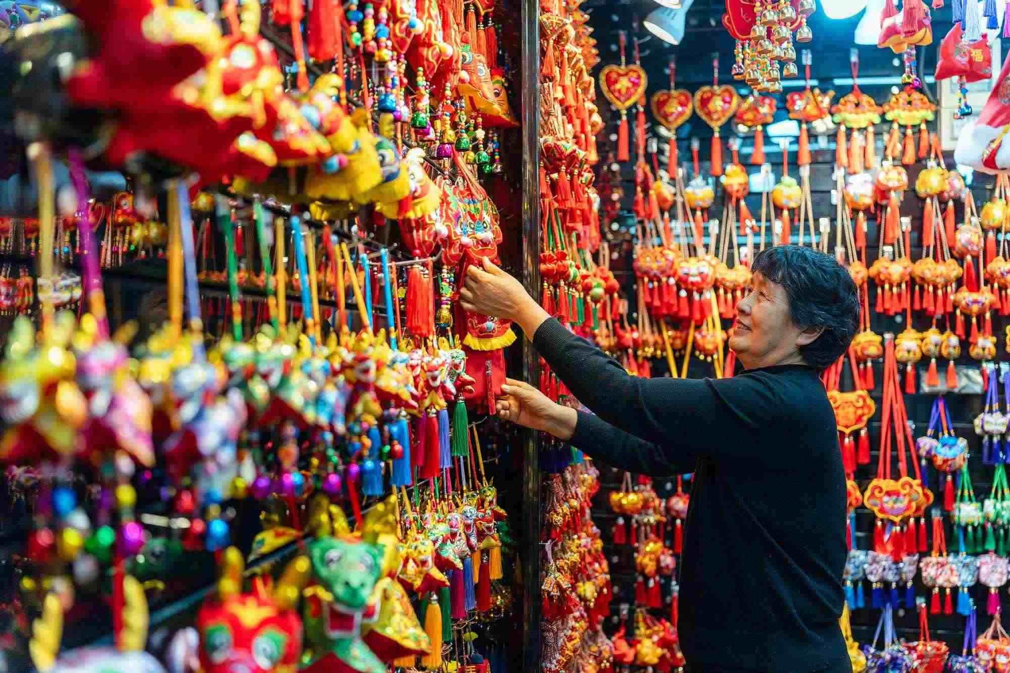 2023年12月11日，金華義烏國際商貿(mào)城，龍年喜慶用品掛滿攤位，顧客正在挑選中。