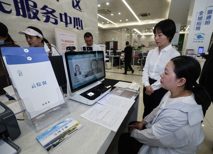 在浙江省嘉興市秀洲區(qū)王江涇鎮(zhèn)便民服務(wù)中心的“跨域通辦·云綜窗”窗口，辦理開業(yè)登記的個(gè)體工商戶（右一）通過(guò)該系統(tǒng)與江蘇省蘇州市吳江區(qū)盛澤鎮(zhèn)行政審批局工作人員視頻連線，進(jìn)行身份讀取及材料線上審核（2024年5月9日攝）。新華社記者 徐昱 攝