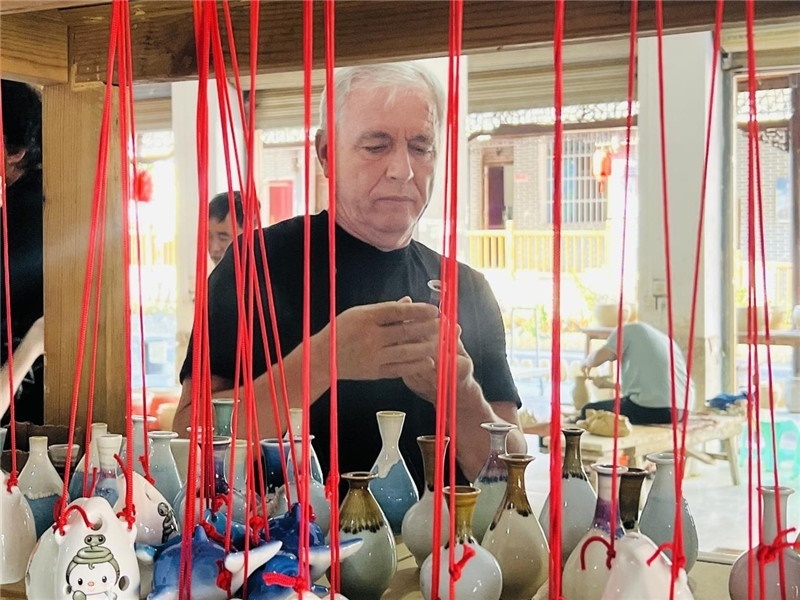 鄉(xiāng)愁如同一根根紅線，將游子與故鄉(xiāng)永遠(yuǎn)地牽連到一起。花茂村陶藝文化創(chuàng)意一條街的母氏陶藝館內(nèi)，紅線吊著陶瓶，思緒游走萬里。摩爾多瓦“信息標(biāo)簽”通訊社社長亞歷山大·塔納斯端詳著館內(nèi)展示的陶藝作品，并挑選出心儀的小擺件帶回摩爾多瓦，也帶走花茂村的“鄉(xiāng)愁”。（張亞欣攝）