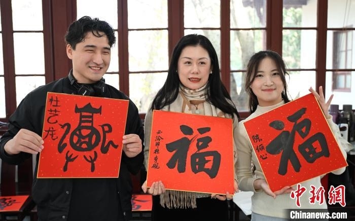 1月20日，外籍留學(xué)生和西泠印社社員李硯(中)展示各自創(chuàng)作的福貼。當(dāng)日，來(lái)自巴西、馬來(lái)西亞、加納、哈薩克斯坦的外籍留學(xué)生在浙江杭州西泠印社體驗(yàn)福貼、春聯(lián)和篆刻，感受古老的中國(guó)傳統(tǒng)文化。中新社記者 王剛 攝